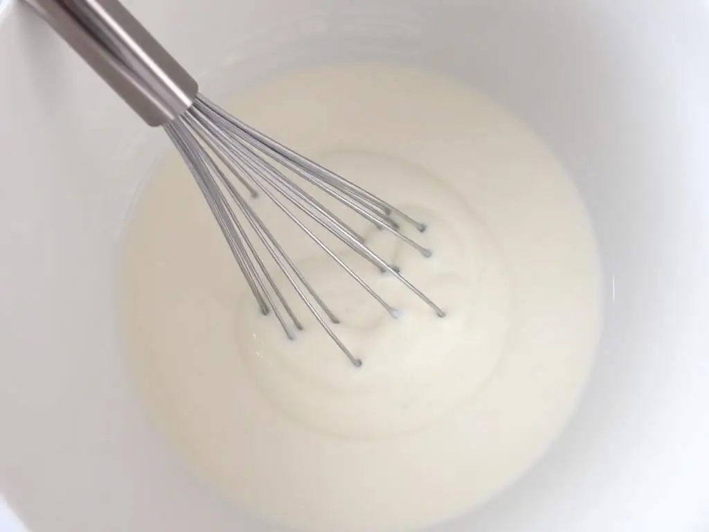 Jogurt naturalny mieszany z wodą w misce - przygotowanie zamiennika maślanki Jogurt naturalny mieszany z wodą w misce - przygotowanie zamiennika maślanki